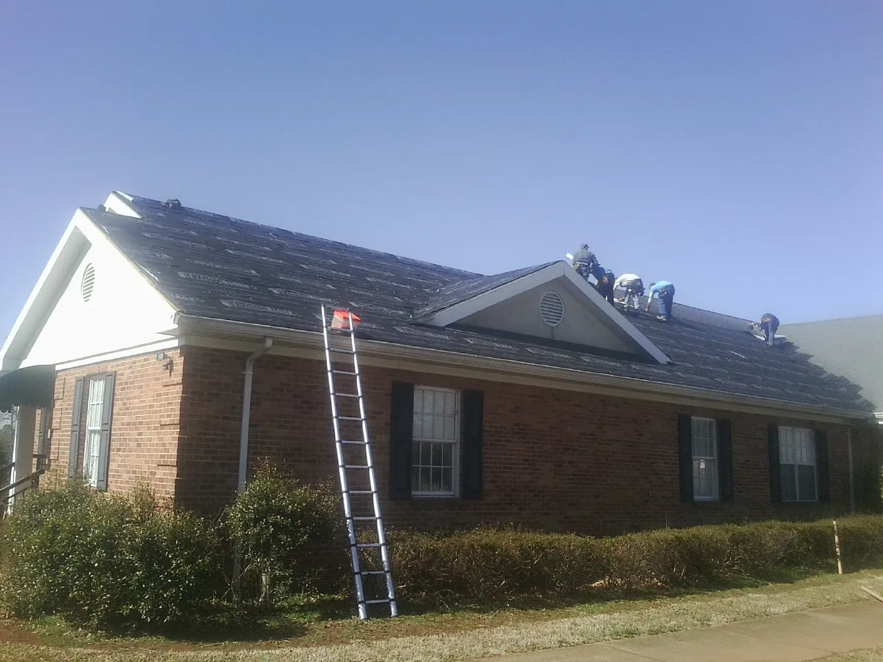 Crew tearing shingles off a brick ranch roof with a ladder set — Metal Roof Repair work by our crew in Clovis
