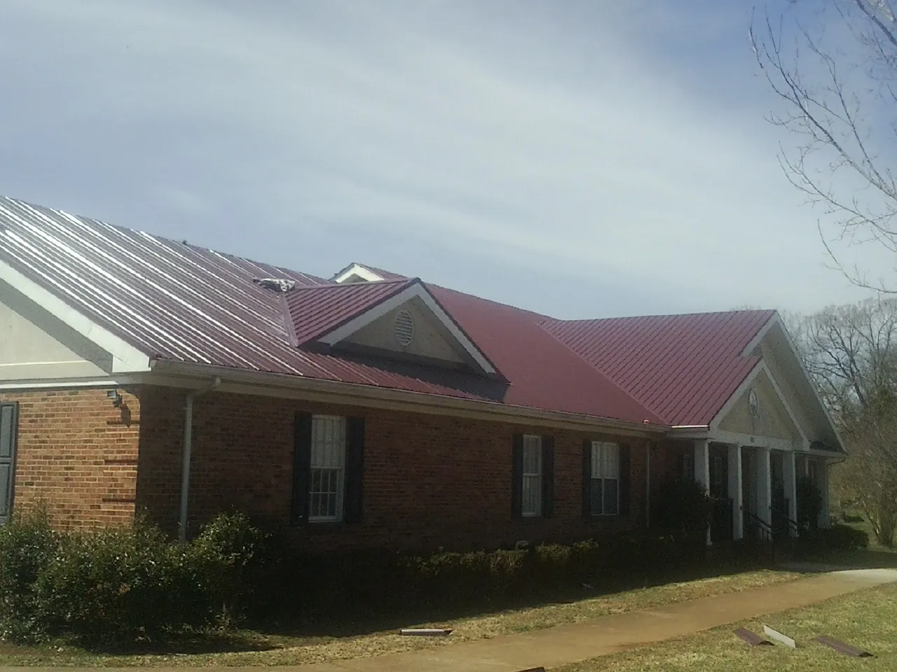Red metal roof with gabled entries on a long brick building, from a Hail Damage Roof Repair job in Clovis