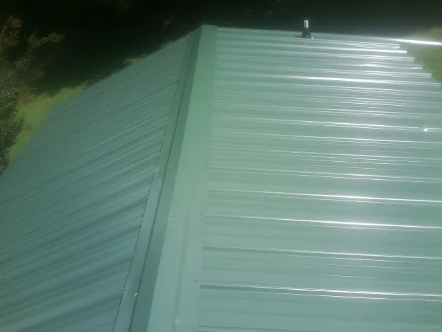 New green metal panels meeting at the ridge of a roof — Flat Roof Repair work by our crew in Clovis