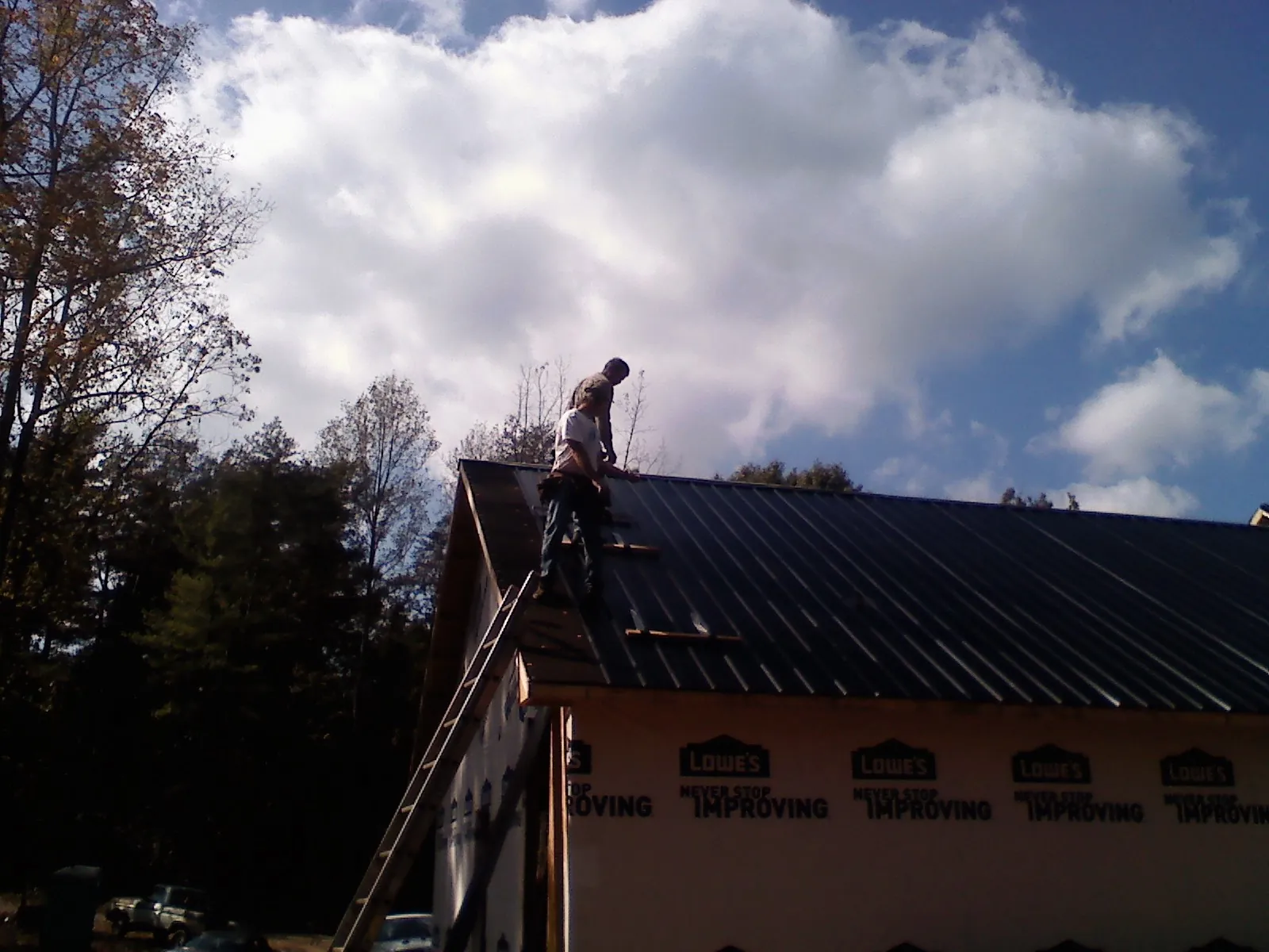 Roofer fastening dark metal panels high against a cloudy sky, from a Roof Inspection job in Clovis