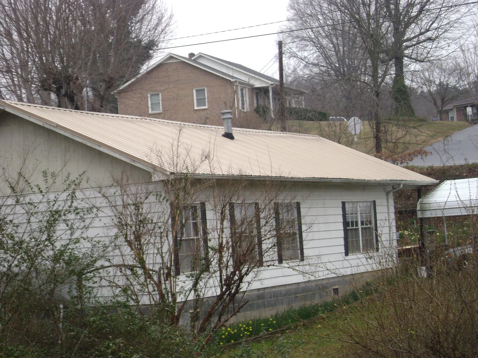 Tan metal roof on a white sided house set into a hillside — Commercial Roofing by Roofing Brothers in Clovis